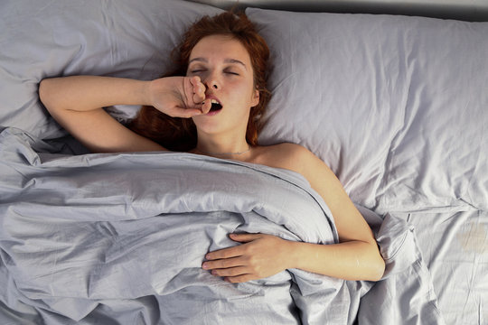 Red head girl yawning in gray bed