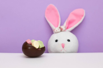 A chocolate egg filled with candy and a rabbit's head peeking from the table