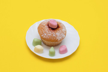 Cupcake and candy on a saucer on a yellow background