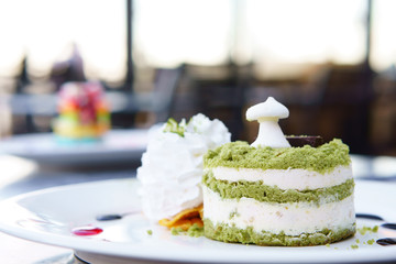 green tea cake with mousse cream on white dish in bakery for herb sweet dessert or snack and delicious on nature warm sunlight for breakfast or morning food at coffee shop or cafe restaurant