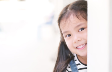 Asian child curious or kid girl playing peekaboo or hide and seek with sneaked or dodge behind post and happy smiling white teeth or cheerful at public park or playground on relax holiday with space © kornnphoto