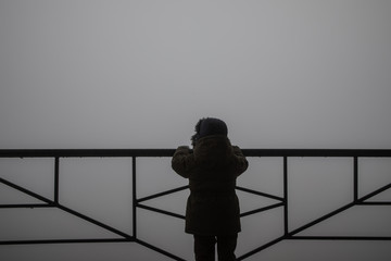 silhouette of a child holding handrail and looking towards fog mist