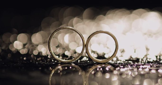 Wedding rings lying on dark surface shining with light close up macro. Reflection. Black background