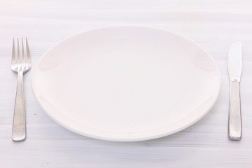 白い木製テーブルに置かれた白い皿とカトラリー