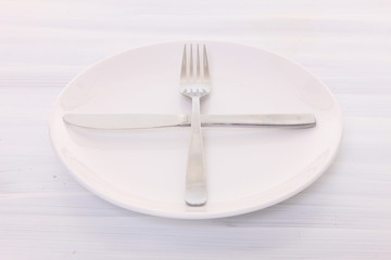 白い木製テーブルに置かれた白い皿とカトラリーによる次の料理を待機の合図