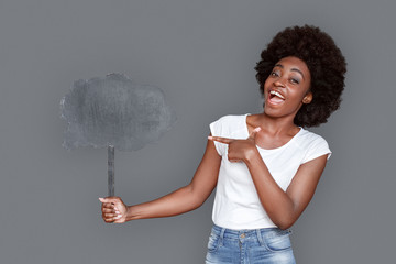 Young woman standing isolated on gray pointing at cloud looking camera excited