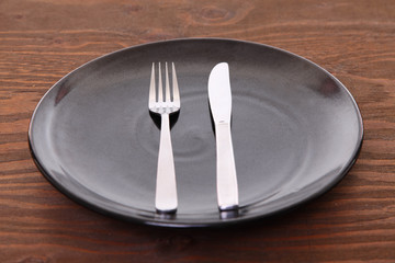 茶色い木製テーブルに置かれた黒い皿とカトラリーによる食事終了の合図