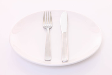 白いテーブルに置かれた白い皿とカトラリーによる食事終了の合図