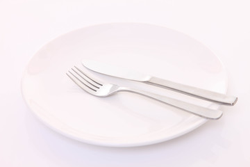 白いテーブルに置かれた白い皿とカトラリーによる食事終了の合図