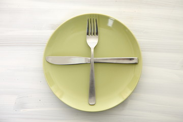 白い木製テーブルに置かれた緑の皿とカトラリーによる次の料理を待機の合図