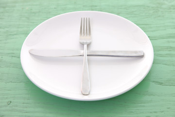 緑の木製テーブルに置かれた白い皿とカトラリーによる次の料理を待機の合図