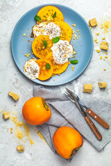 Sliced persimmon with yogurt, chia seeds, brown sugar, pine nuts and fresh mint