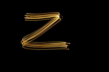 Long exposure, light painting photography.  Letter z in a vibrant neon metallic yellow gold colour against a black background.  Alphabet series.