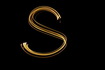 Long exposure, light painting photography.  Letter s in a vibrant neon metallic yellow gold colour against a black background.  Alphabet series.