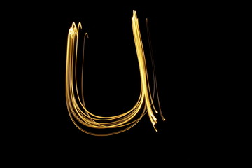 Long exposure, light painting photography.  Letter u in a vibrant neon metallic yellow gold colour against a black background.  Alphabet series. © LizFoster