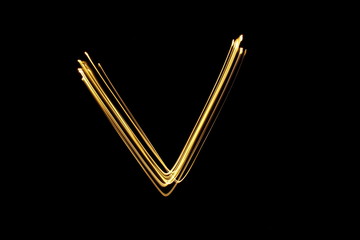 Long exposure, light painting photography.  Letter v in a vibrant neon metallic yellow gold colour against a black background.  Alphabet series.