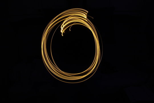 Long exposure, light painting photography.  Letter o in a vibrant neon metallic yellow gold colour against a black background.  Alphabet series.