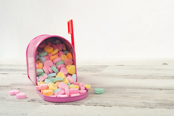 Pink mailbox full of candy conversation hearts on a wood table with a shallow depth of field and copy space