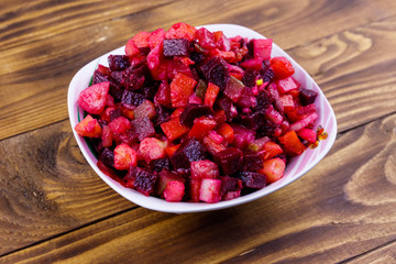 Traditional russian salad vinaigrette with beetroot, carrot, potato, onion and pickled cucumbers on wooden table