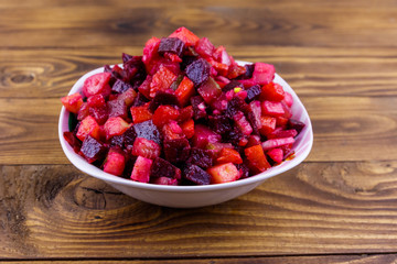 Traditional russian salad vinaigrette with beetroot, carrot, potato, onion and pickled cucumbers on wooden table