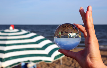 hand with big crystal ball on the beach with parasol by the sea