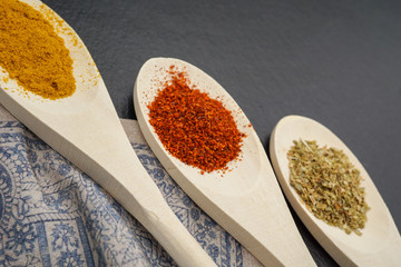 Spices in wooden spoons on dark background. Pepper chilly, basil, curry. Concept of organic food. top view.