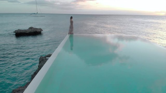 Aerial Forward: Woman Standing on the Edge of Swimming Pool next to the Ocean 