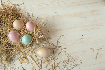 Stack of colorful easter eggs on straw with wooden table background