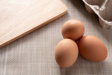Close-up view of fresh brown eggs in the box to prevent it from cracking. Was put on a brown canvas to wait for cooking with a wooden cutting board placed beside.