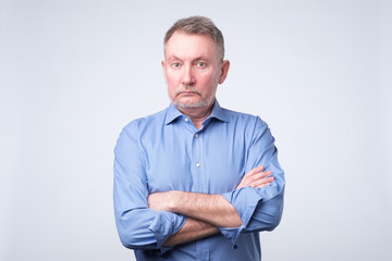 Serious senior man with folded arms and a deadpan expression posing on grey wall