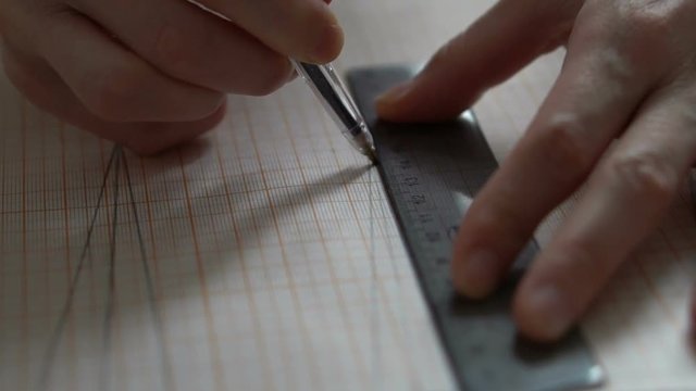 Woman's hands draw with a pen on graph paper. Clothing design in the workshop. Slow motion.