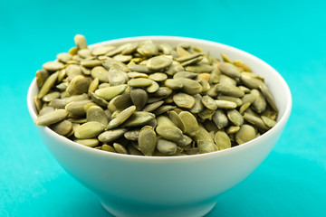 Bowl full of pumpkin seeds on turquoise background