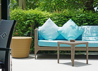 Blue cushion wicker sofa bench in small modern garden outdoors.