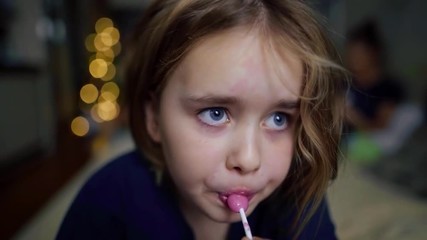 a little girl lying on the couch licking lollipop.