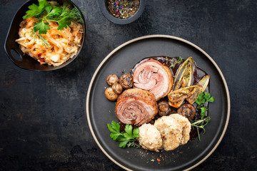 Traditional rolled boar roast with dumpling, fried vegetable and mushroom as top view on a modern design plate with game red wine sauce