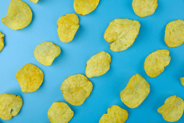 Yellow potato chips on light pastel blue background. Snacks pattern. Top view
