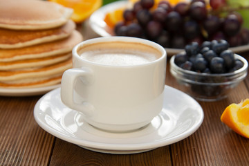 Healthy breakfast. Deliciouse homemade american pancakes with cup of coffee and fruits. Wooden table, beautiful morning in garden.