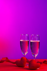 Champagne in glasses of two in romantic valentine concept with heart shaped fabric on red and purple background