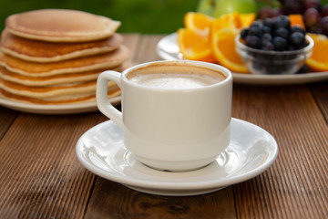 Healthy breakfast. Deliciouse homemade american pancakes with cup of coffee and fruits. Wooden table, beautiful morning in garden.