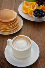 Healthy breakfast. Deliciouse homemade american pancakes with cup of coffee and fruits. Wooden table, beautiful morning in garden.