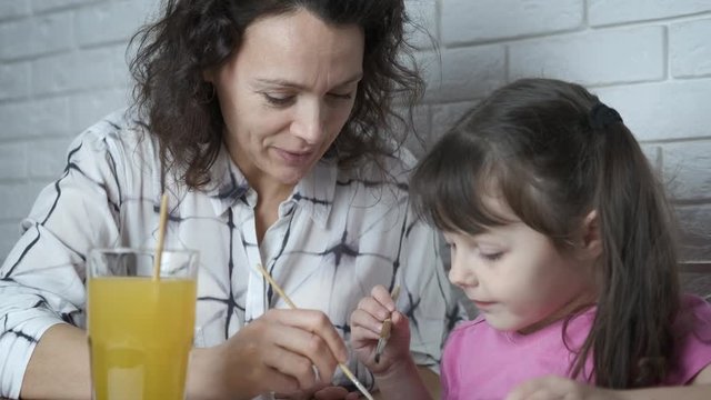 Child draws with mom. A cute mother with her little daughter paint together with paints.