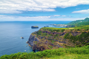 Fototapeta na wymiar Eclectic terrain of coast of Sao Miguel island of Azores, Portugal, with steep rocks and fields covered by greenery.