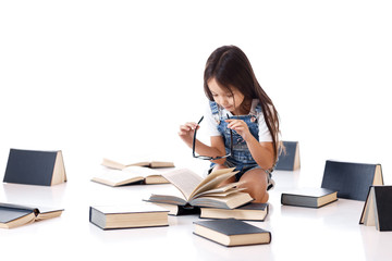 cute little girl in denim and glasse is reading a book. child and a lot of books. Children and education.