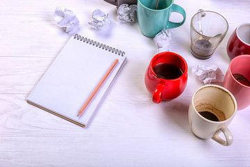 Empty dirty coffee cups, different colors on the table and a notebook for writing a letter. Concept caffeine dope, lack of energy to solve the problem. Copy space.