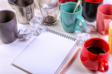 Empty dirty coffee cups, different colors on the table and a notebook for writing a letter. Concept caffeine dope, lack of energy to solve the problem. Copy space.