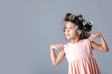 Funny cute little child girl in pink dress and hair curlers posing on gray background. Human emotions and facial expression