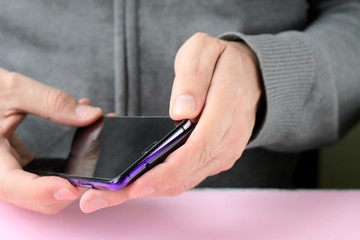Male hands are holding a phone and putting on a shiny colorful cover. White man in a gray sweater put on a new violet case on smartphone with selective focus. Plastic case for digital gadget