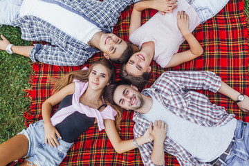 Two beautiful girls with  their handsome boys sitting in a park on a blanket and looking to the camera