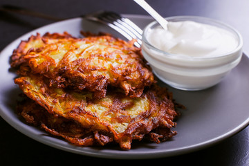 Hash brown and sour cream on a plate on a dark stone background, well fried. Copy space.