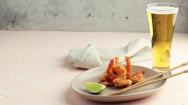 Fried Shrimps tempura with lime in light plate and pouring beer in glass on pink concrete surface background. Copy space Seafood tempura dish served japanese or eastern Asia style with chopsticks
